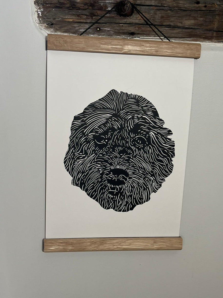 Black and white illustration of a dog's face on a white sheet of paper with a wooden frame, hanging on a light gray wall.